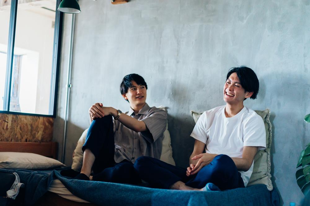 室内で壁に寄りかかって談笑する男性2人